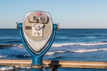 Coin-operated binoculars on a fishing pier with a view of ocean waves in the distance. 