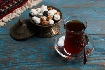 Turkish tea in traditional glass and copper bowl with sweet snacks on rustic wooden table background, close-up