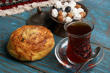 Gogal and glass of black tea with traditional snack in copper bowl, on rustic wooden table. Azerbaijan national Novruz holiday pastry 