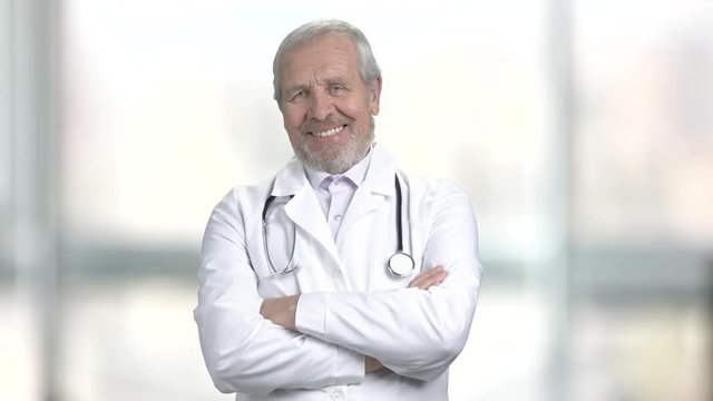 Smiling doctor crossed arms on blurred background. Portrait of happy ederly doctor folded arms on abstract blurred background.