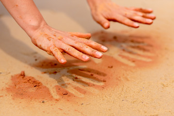 Woman hands creating shapes with red sand on the beach in aboriginal art style - 196808956