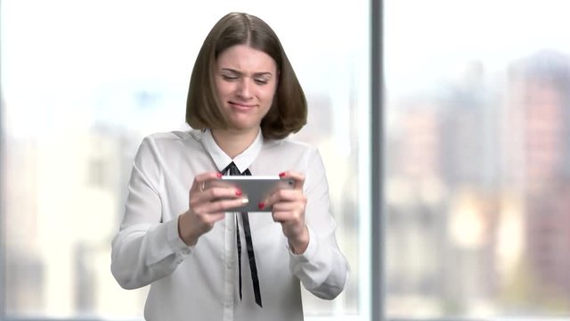 Young joyful woman playing on smartphone. Funny business woman playing online game on phone, blurred background. Female corporate having a break.
