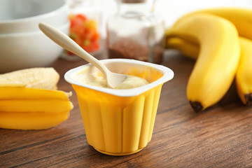 Plastic cup of yummy banana yogurt on wooden table