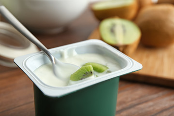 Plastic cup of yummy kiwi yogurt on wooden table, closeup