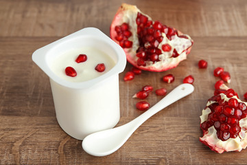 Plastic cup of yummy yogurt with pomegranate seeds on wooden table