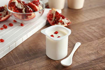 Plastic cup of yummy yogurt with pomegranate seeds on wooden table