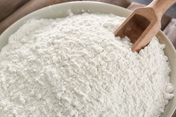 Wheat flour and wooden scoop in bowl, closeup