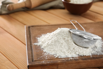 Wheat flour and sieve on wooden board
