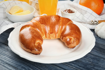 Plate with fresh tasty crescent roll on wooden table