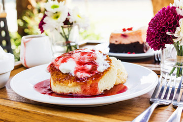 Cheese cake topping strawberry jam on wooden table under tree shade and garden background