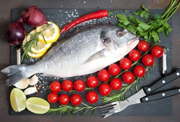 raw fish  Dorado  with spices and vegetables on slate plate