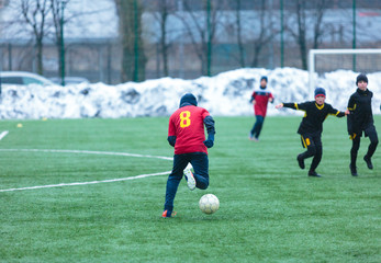 Obraz premium boy in red uniform -football player plays soccer on the green field in the winter