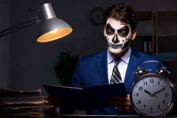 Businessman with scary face mask working late in office