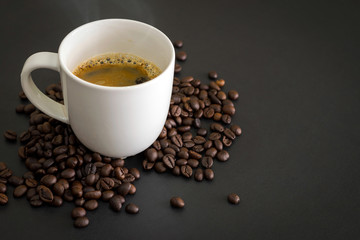 Hot coffee in white ceramic glass and coffee beans placed on the black table.