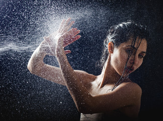 young girl portrait and splashing water in her face. beautiful female model on black background.