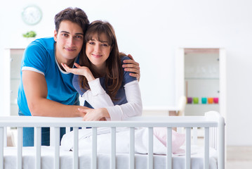 Happy young family at baby bed cot