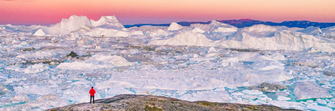 Greenland travel hiker tourist man trekking at sunset. Adventure expedition in the arctic ocean, ice floating from icebergs in ocean. Banner panorama.