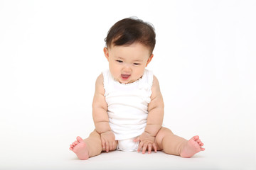 白バックの前に一人座り遊ぶ女の子の赤ちゃん