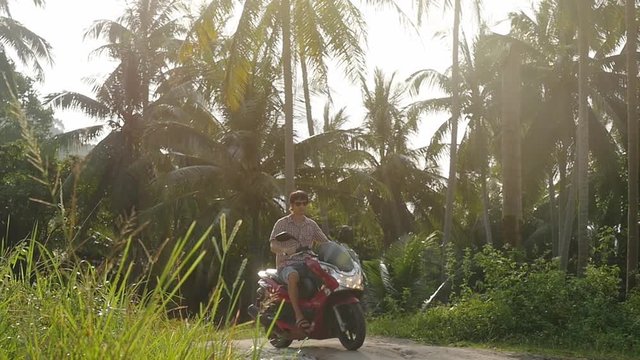 Young handsome man traveler in sunglasses driving motorbike on tropical sunny road. slow motion. 1920x1080