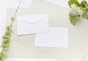 Craft paper sheets and white envelope. Blank card with spring green leaves and white flowers. Mockup design. Top view with copy space.