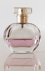 Glass bottle with pink perfume close-up on beige background.