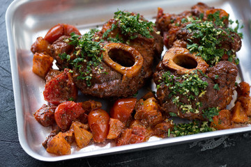 Osso buco made of cross cut veal shank with oranges, tomatoes and gremolata on a baking tray, closeup