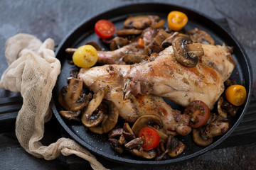 Cast-iron pan with roasted rabbit, champignons and fresh cherry tomatoes, studio shot