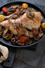Roasted rabbit with fried mushrooms and fresh cherry tomatoes in a cast-iron pan, close-up, vertical shot