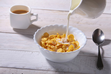 Milk pouring into a bowl of delicious corn flake cereals and cap with espresso coffee. Morning breakfast.