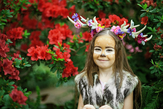 Fairy tale girl. Portrait a little girl in a deer dress with a painted face in the forest. Big brown antler