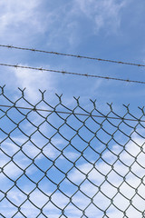 barbed wire security fence in a blue cloudy sky