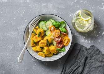 Crispy baked slices of polenta with sage butter and vegetables cucumbers, tomatoes, basil salad on a gray background, top view. Vegetarian food © okkijan2010