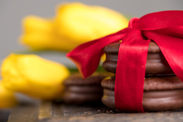 Chocolate biscuits with a delicate filling and a tulip flower. A gift for Valentine's Day. Chocolate biscuits, tied with satin red ribbon. Macro.