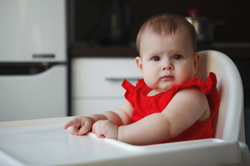 baby in a red dress is sitting on a child's chair