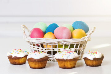 Fototapeta na wymiar Holiday Easter concept. Multicolored easter eggs in a basket, sweet cupcakes. Easter background. Treats for the spring religious Christian holiday
