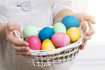 Fototapeta na wymiar Easter concept. A woman holds basket with colorful colored eggs for religious Easter holiday. Easter eggs in basket.