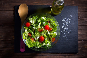 Fresh salad in glassy bowl on black stone plate on wooden table