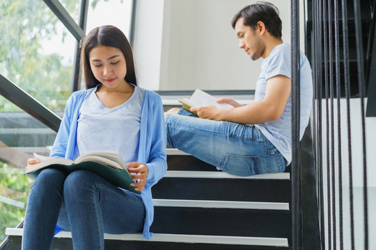 Young asian couple reading book on stairs at home. concept of knowledge examination intelligence research and education.