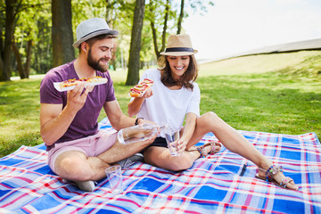 Young couple out on picnic in park together eating and pouring water into glass