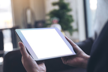 Mockup image of hands holding black tablet pc with blank white desktop screen in the house