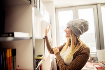 Young cheerful student girl with hat choosing book from the bookstore.