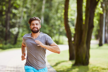 Smiling young man running in the park during summer