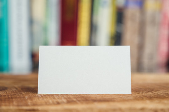 The empty white business card on wooden table and blur bookshelf in background