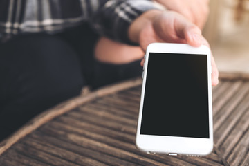 Mockup image of a hand holding and giving white mobile phone with blank black desktop screen to someone in cafe