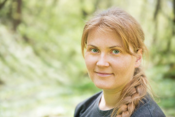 Portrait of young woman with red hair and plait in the green forest