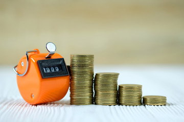 Tally counter or counting machine with 0000 number, step of coin stack on white wooden table, business and finance concept.