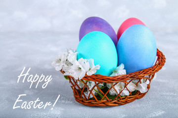 Colored Easter eggs in a basket on a gray concrete background.