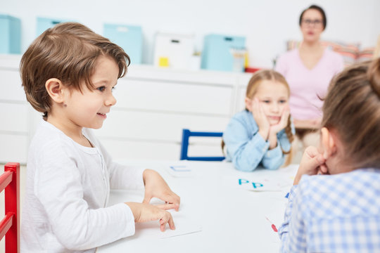 Little Elementary School Learner Listening To One Of Groupmates At Lesson Of English Language