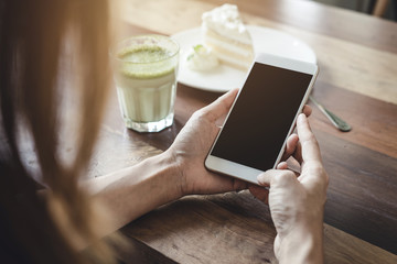 Young woman using smart phone and eating cake in cafe