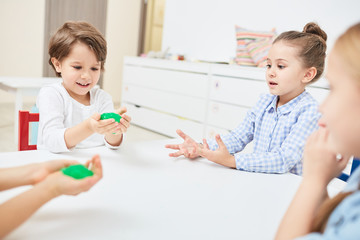 Group of four little kids playing with slimes by table in kindergarten